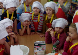 Grupa dzieci zebrana wokół produktów do wykonania piernikowego ciasta.